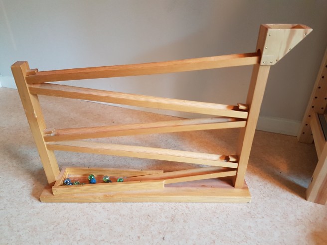 En kulbana i trä. Man lägger i kulorna längst upp och så åker kulorna i banor fram och tillbaka tills den stannar längst ner.