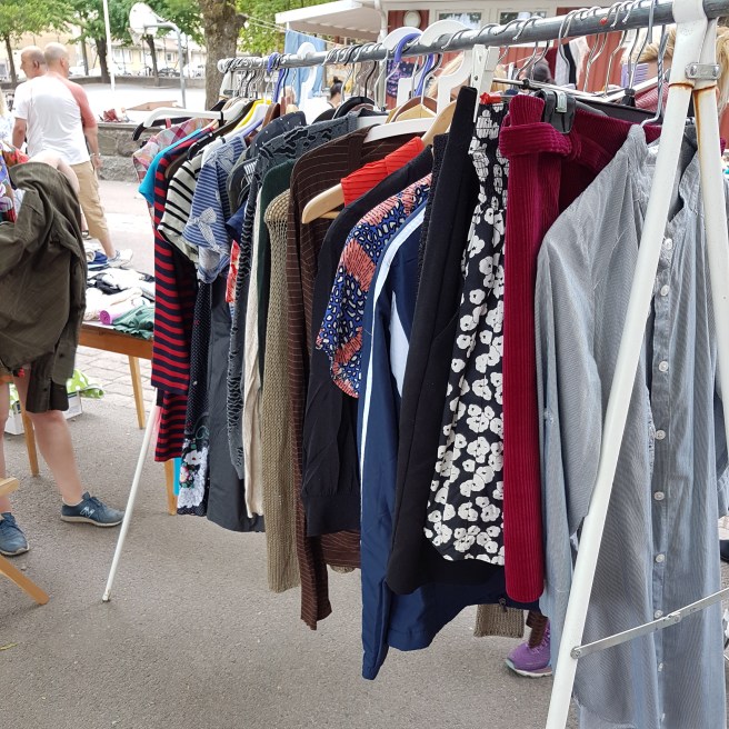 En klädhängare med kläder som en person säljer på loppmarknaden.